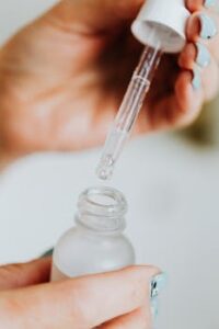 Hand holding a dropper, applying microdose THC  from a frosted glass bottle, close-up view.