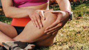Close-up of a woman sitting cross-legged on grass, holding her knee, wearing a smartwatch.