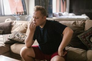 Cannabis as a Natural PTSD Treatment: Adult man sitting indoors, smoking a joint, in a relaxed setting.