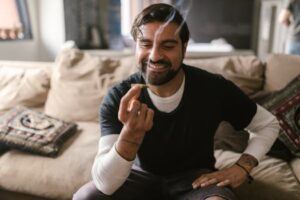 Smiling man holding a cannabis joint, seated comfortably in a cozy indoor setting.